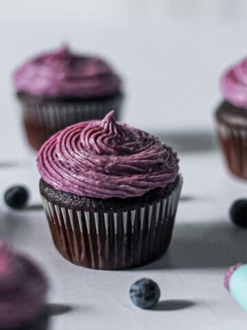 Up-close shot of a chocolate cupcake, topped with a vibrant purply blueberry cream cheese frosting.