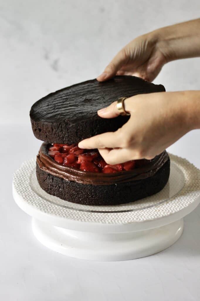 stacking second layer onto chocolate cake with strawberry filling