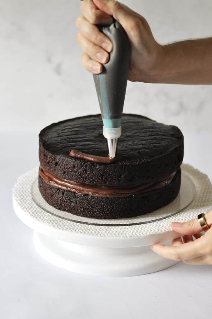 piping ganache onto chocolate layer cake