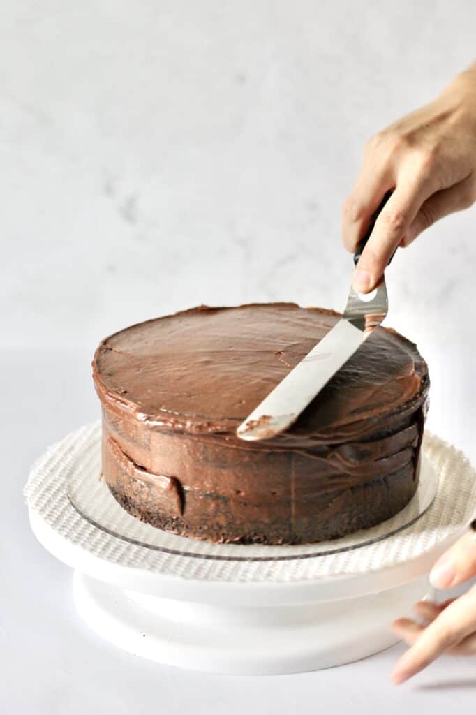 spreading out frosting on chocolate layer cake with a cake spatula
