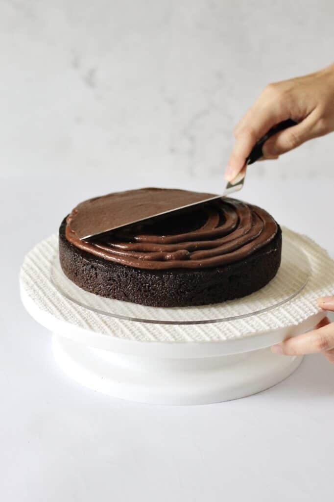 spreading chocolate frosting onto first layer of chocolate cake