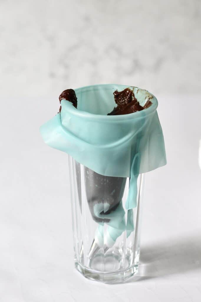 chocolate cake frosting in a piping bag, fitted over the rim of a tall glass
