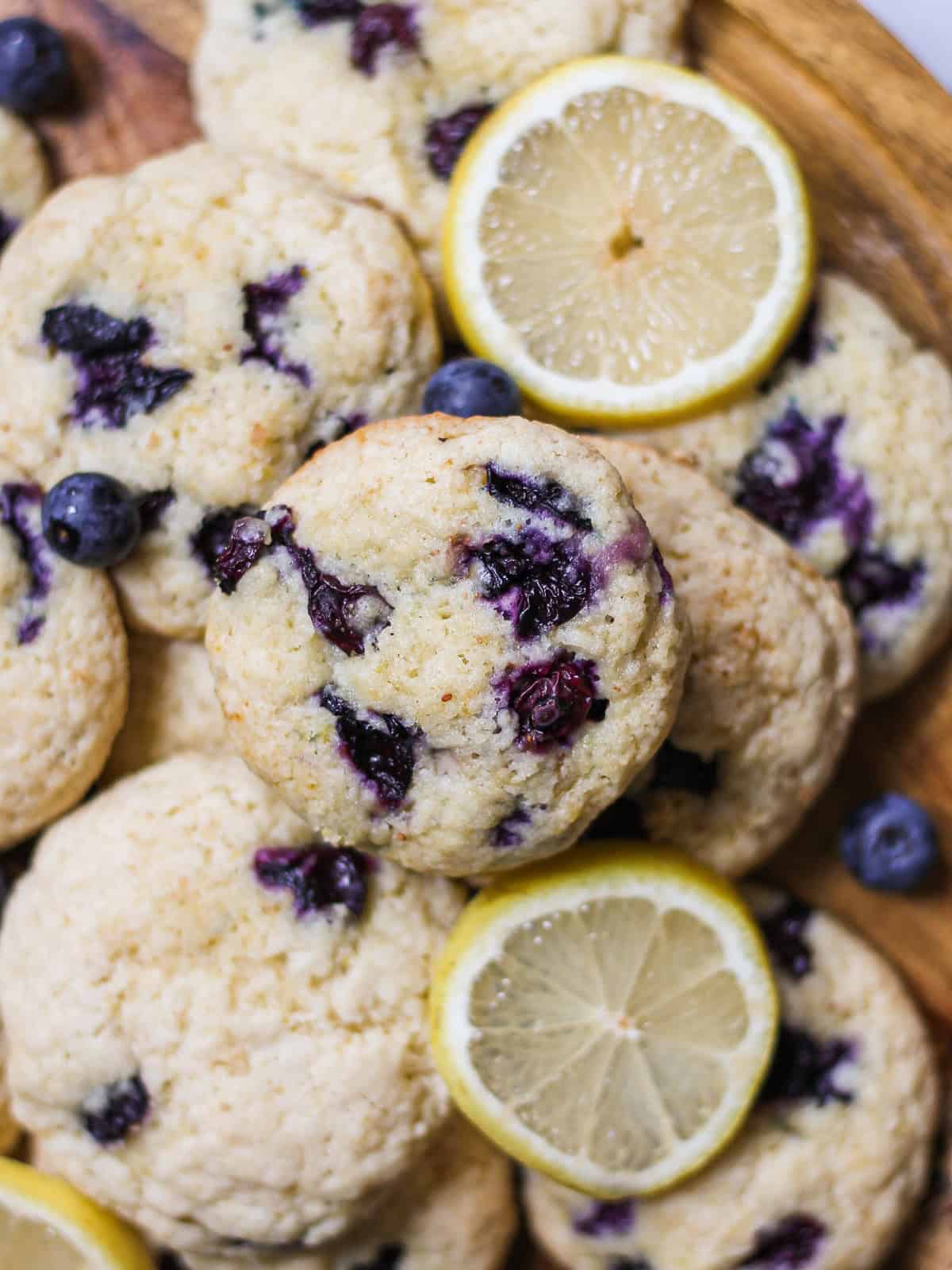 Pile of baked blueberry lemon cookies, sitting on a wooden cake stand.