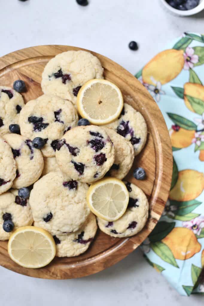 overhead shot of baked blueberry cookies on a wooden cake stand with lemon apron in the background