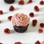 raspberry cream cheese frosting on a chocolate cupcake, surrounded by fresh raspberries