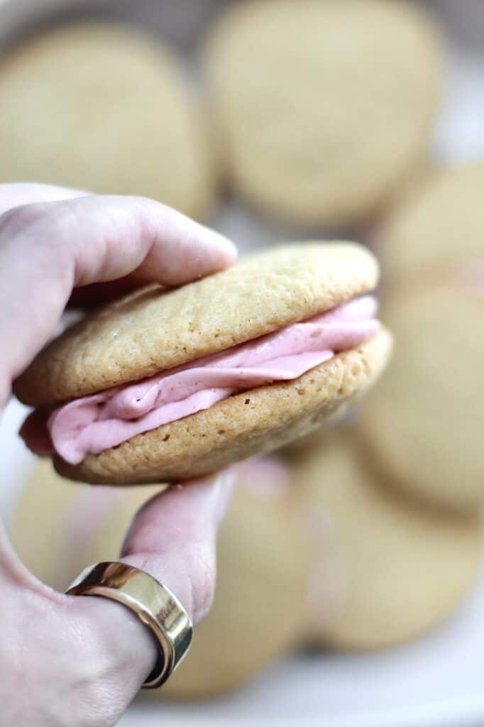 hand holding a cookie sandwich with pink frosting between the layers