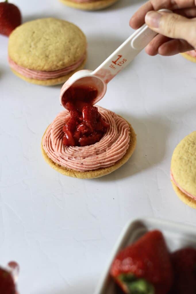 adding filling to assembling strawberry cookie sandwich