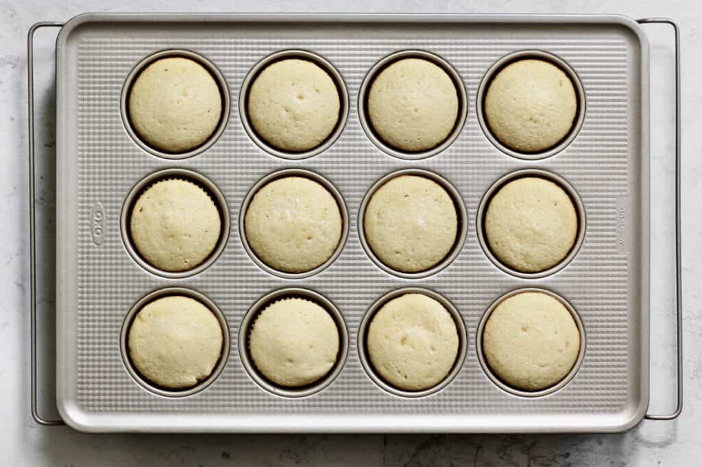 overhead shot of baked vanilla cupcakes in a light-colored muffin tin