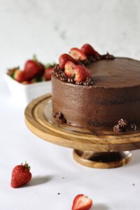 chocolate layer cake with strawberry filling inside it, sitting on a wooden cake stand