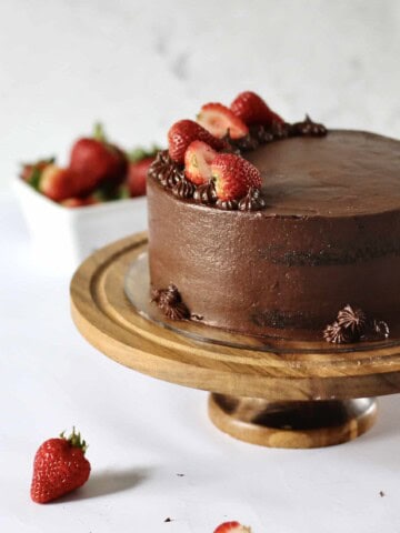 chocolate layer cake with strawberry filling inside it, sitting on a wooden cake stand