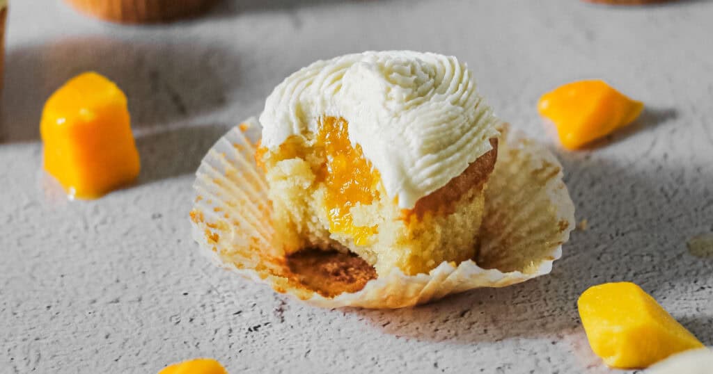 Mango cupcake, missing a bite, and showing the filling inside.