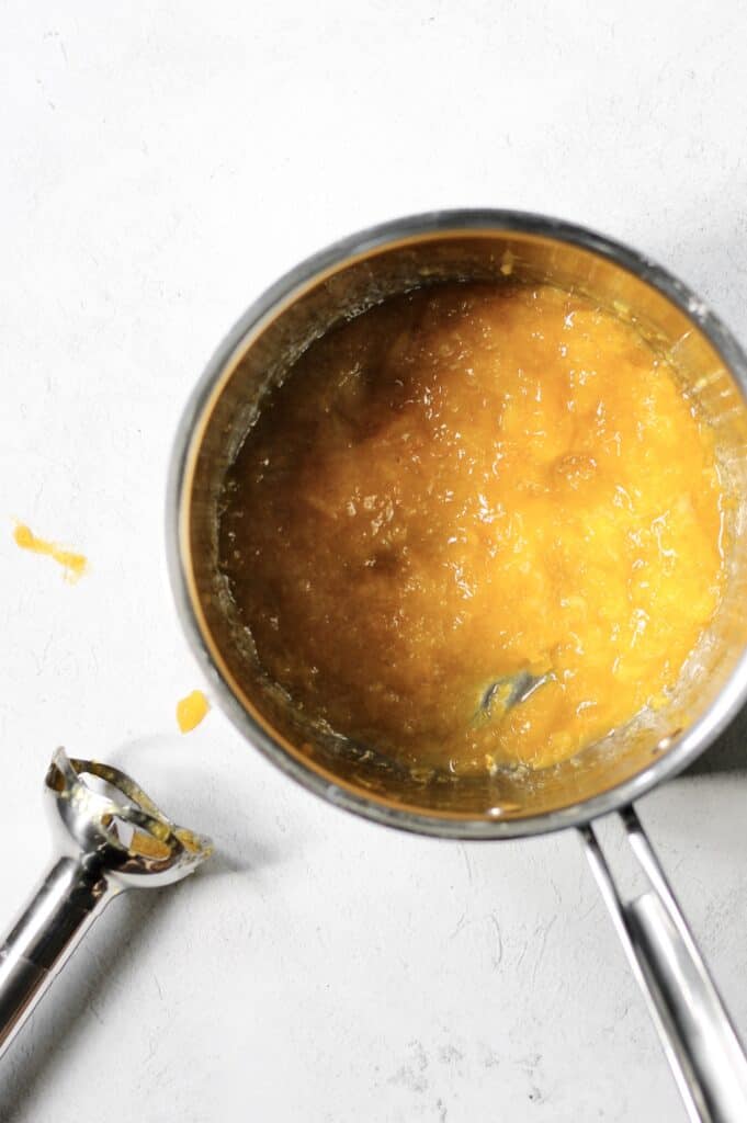 overhead image of mango filling in a pot, next to an immersion blender