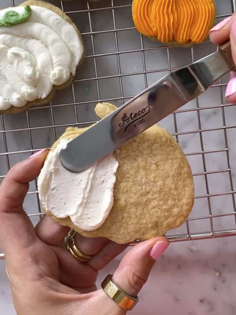 action shot of decorating pumpkin cookie with an offset spatula