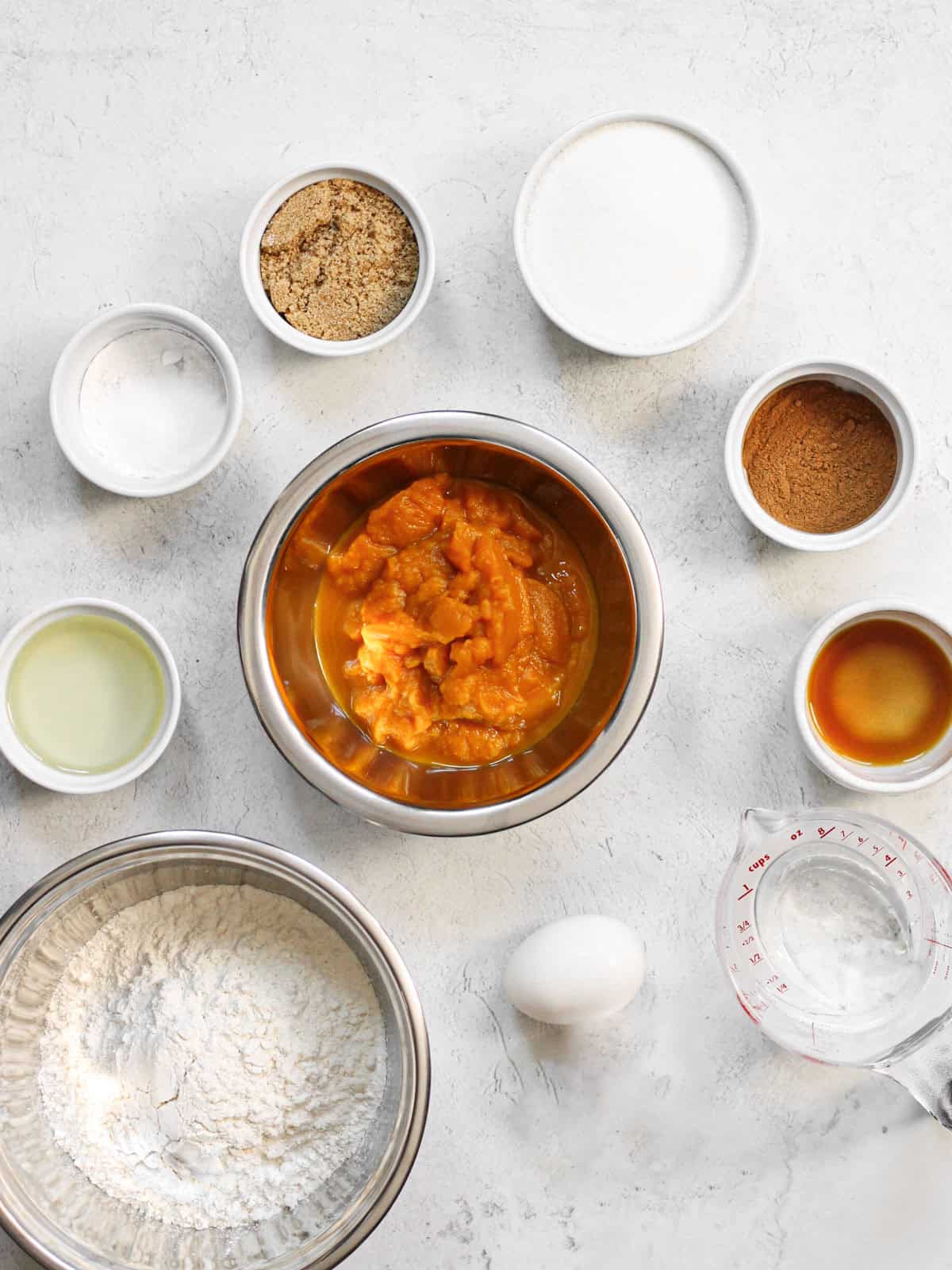 Ingredients for mini pumpkin muffins measured into bowls: flour, sugars, pumpkin puree, oil, egg, and spices.