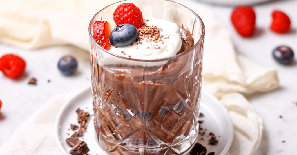 Chocolate mascarpone mousse in a small crystal glass, topped with whipped cream, chocolate shavings, and fresh berries.