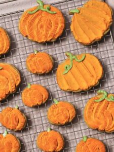 fully decorated pumpkin cookies, coated in orange buttercream, sitting on a cooling rack