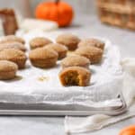Mini cinnamon sugar pumpkin muffins on parchment paper, one broken open, with pumpkins and a basket behind them.