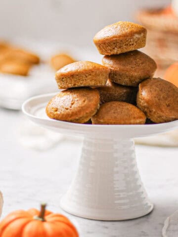 Mini pumpkin muffins stacked in a pyramid shape on top of a white cake stand.