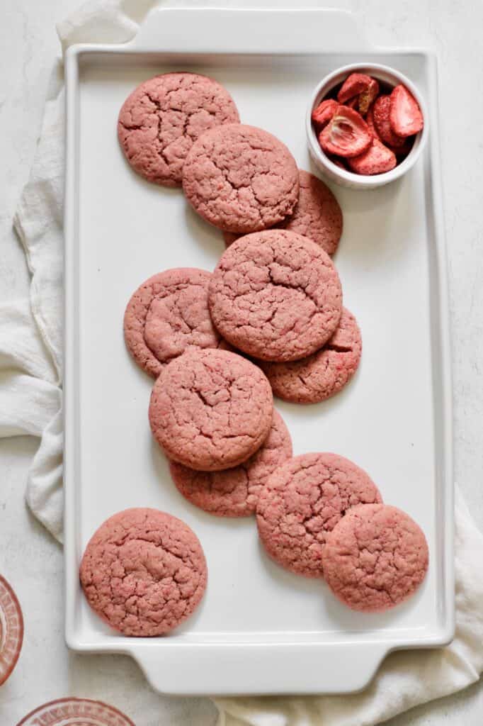 pink sugar cookies on a white platter, with freeze dried strawberries in the upper right-hand corner