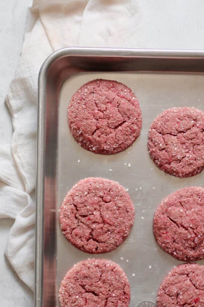 overhead image of pink sugar cookies sitting on metallic cookie sheet, with sparkling sugar on top of them