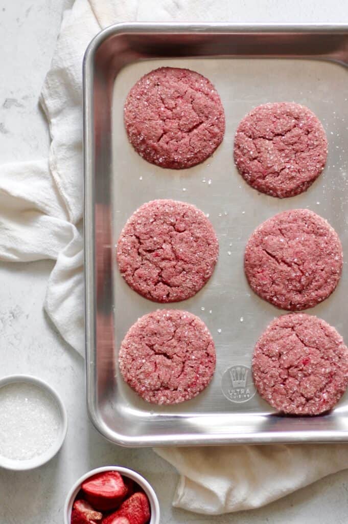 overhead image of pink sugar cookies sitting on metallic cookie sheet, with sparkling sugar on top of them