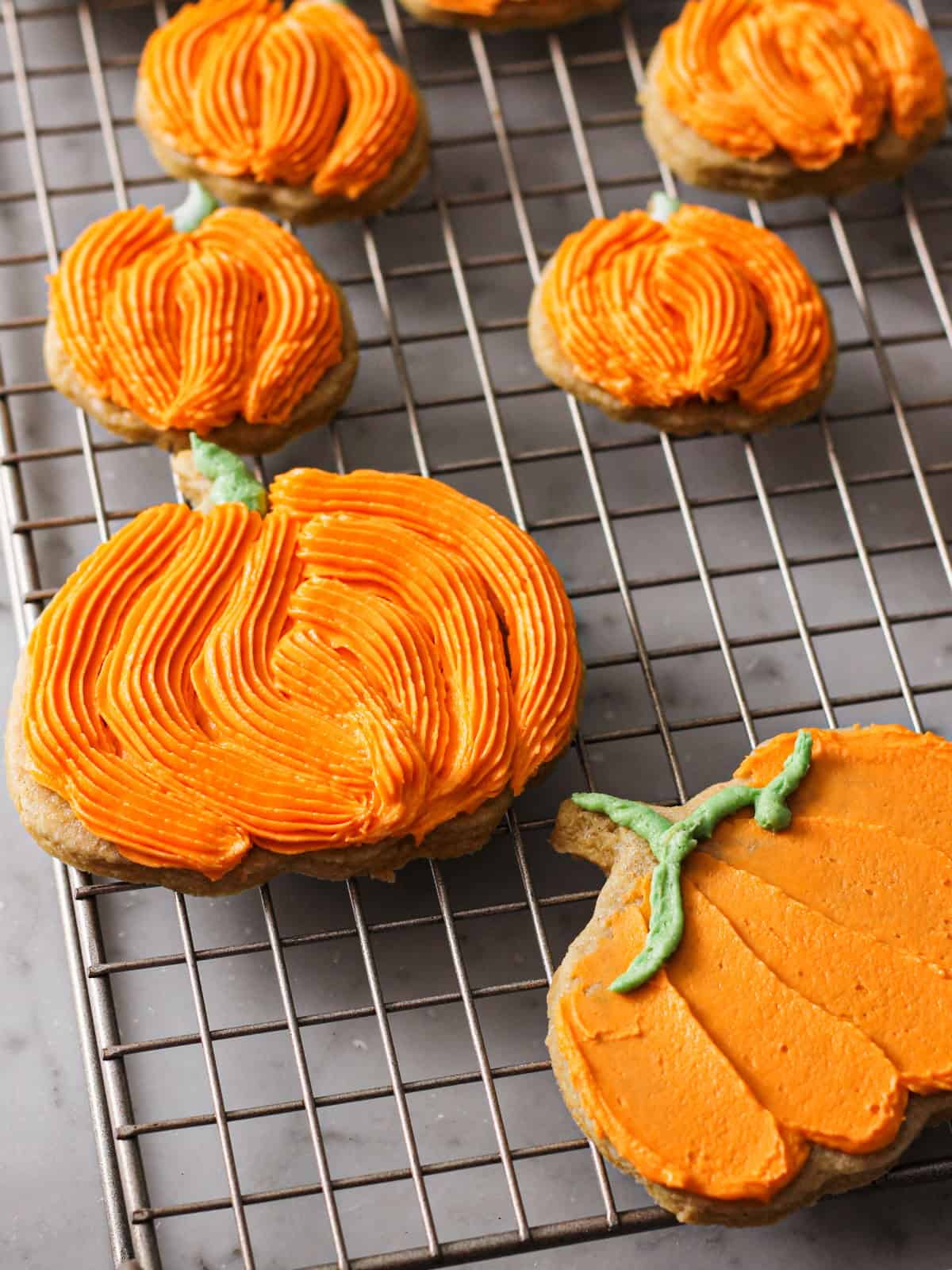 Up-close shot of orange, decorated pumpkin cookies on a cooling rack.