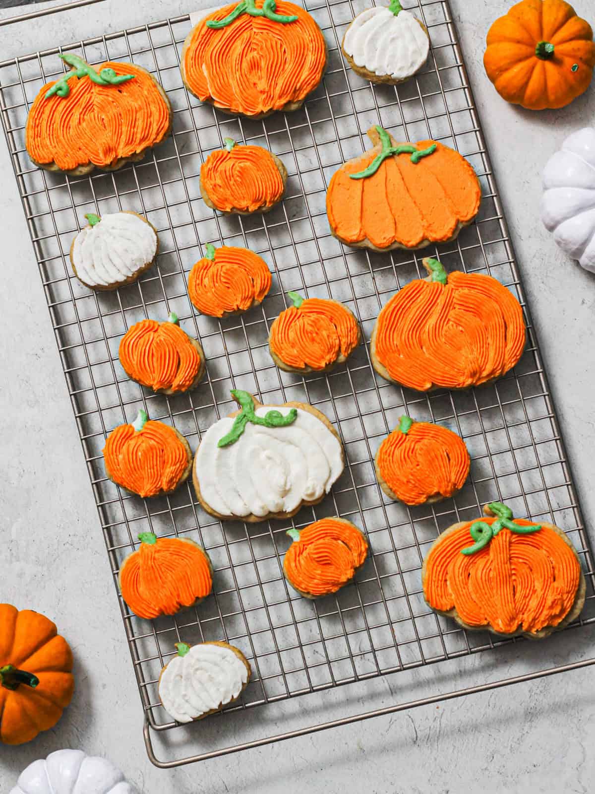Overhead image of mostly orange pumpkin cookies, with a few white ones scattered throughout on a cooling rack.