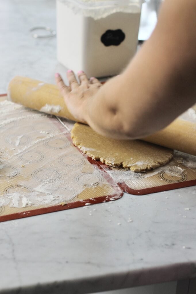 using rolling pin to roll out sugar cookie dough on floured silicon baking mats