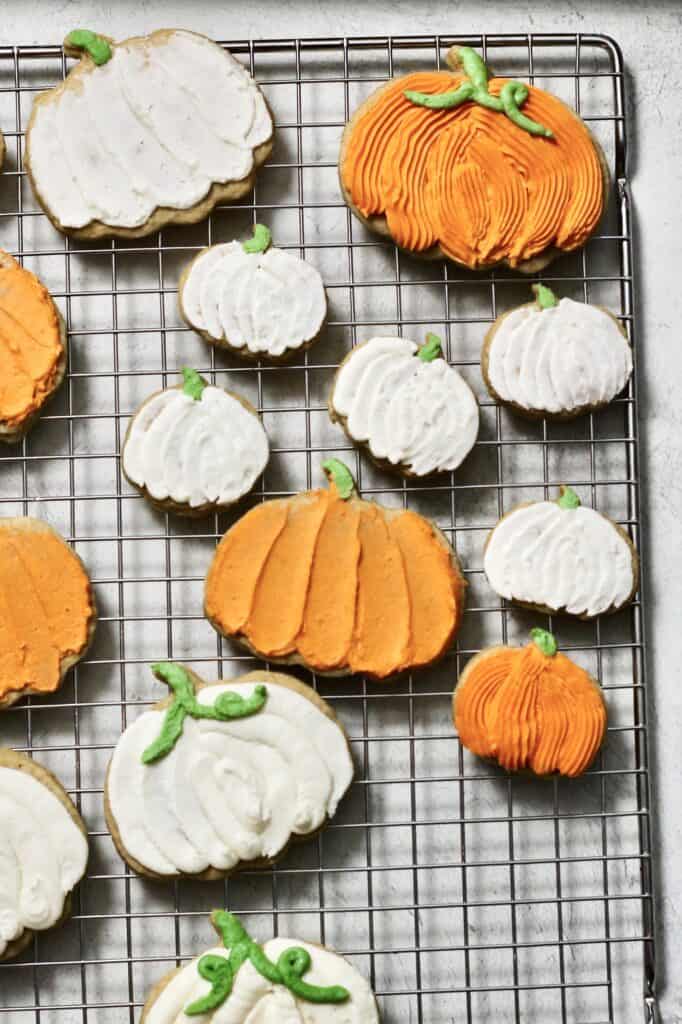 fully decorated pumpkin cookies, coated in orange and white buttercream, sitting on a cooling rack