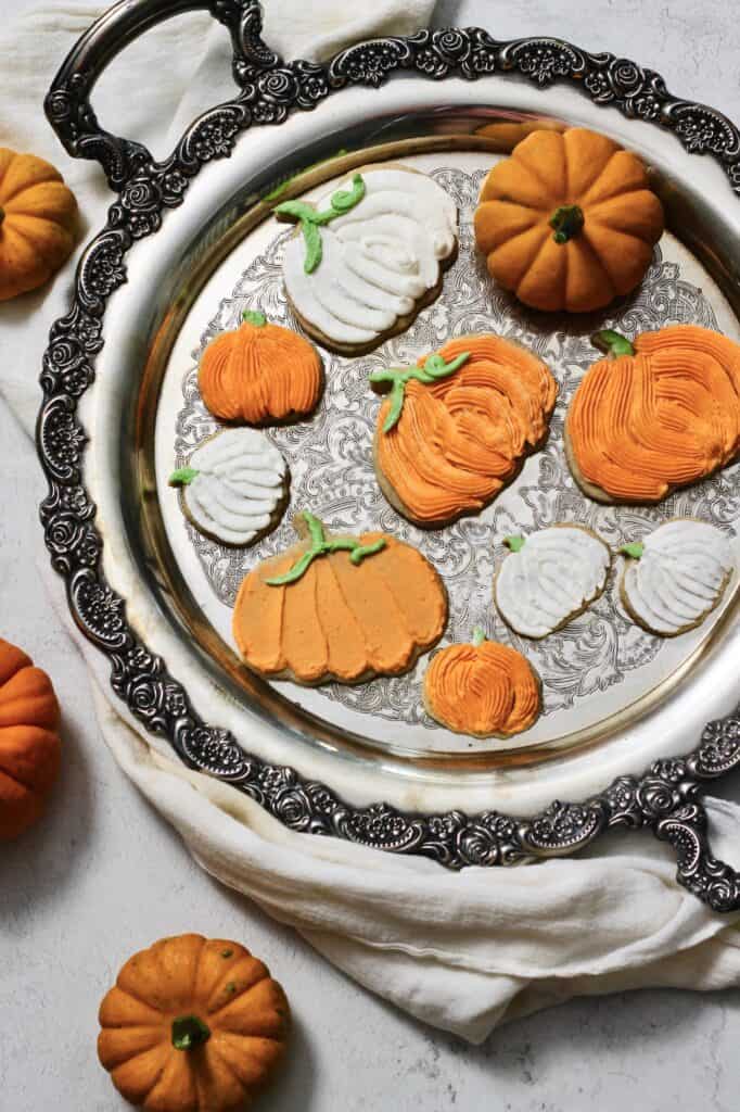 fully decorated pumpkin cookies, coated in orange and white buttercream, sitting on a silver tray