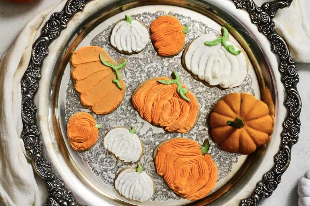 fully decorated pumpkin cookies, coated in orange and white buttercream, sitting on a silver tray