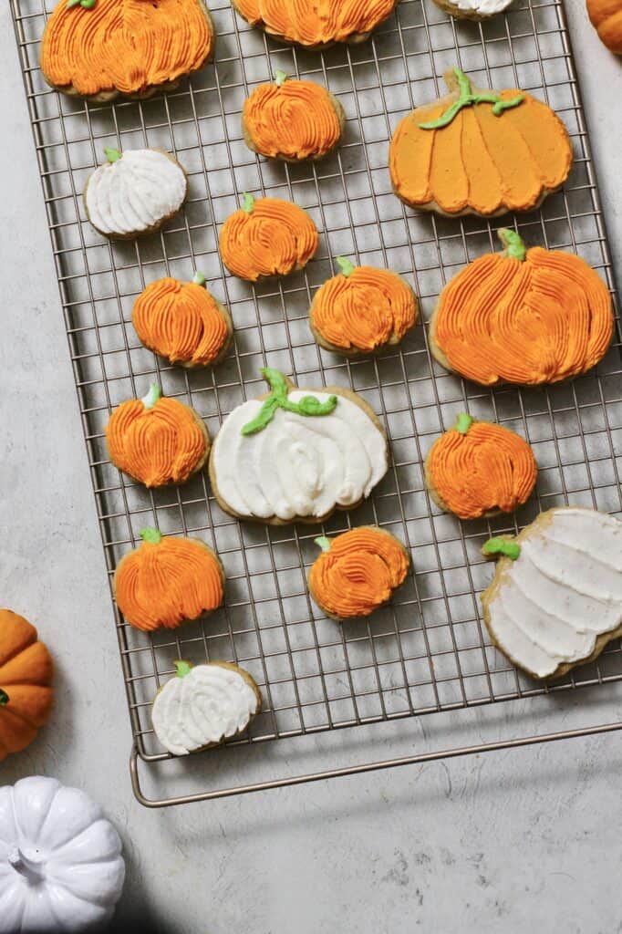 full decorated pumpkin cookies, coated in orange buttercream, sitting on a cooling rack
