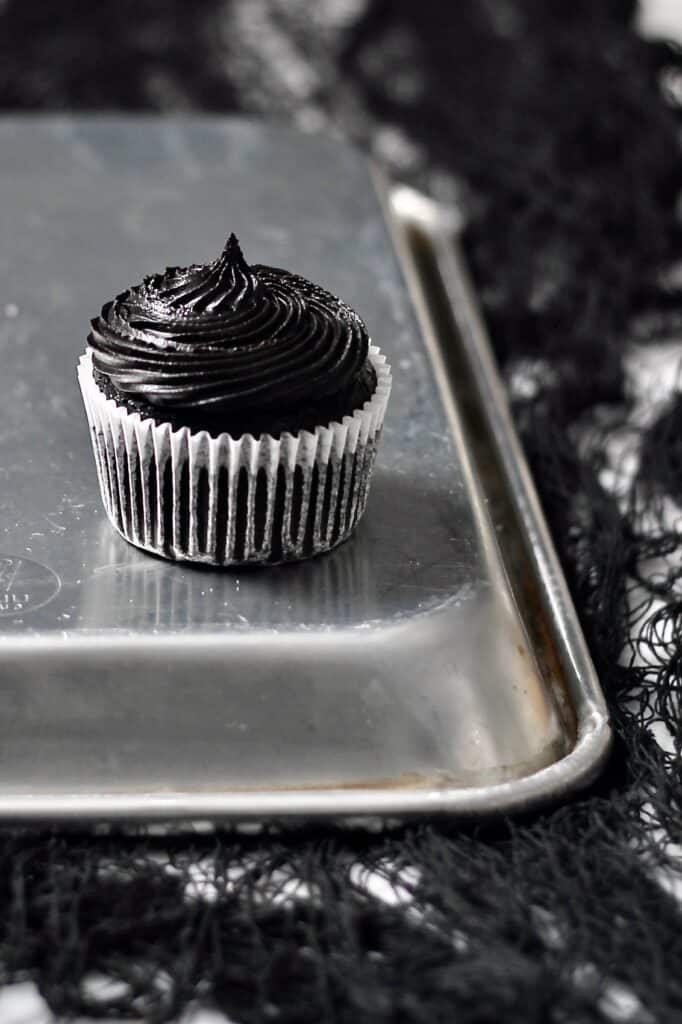 lone black cupcake, sitting on a silver baking tray turned upside down in front of a mostly black background