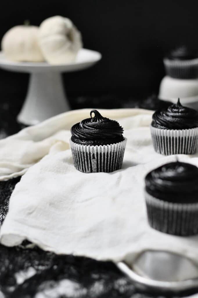 black cocoa cupcakes sitting on a white linen material in front of a black background