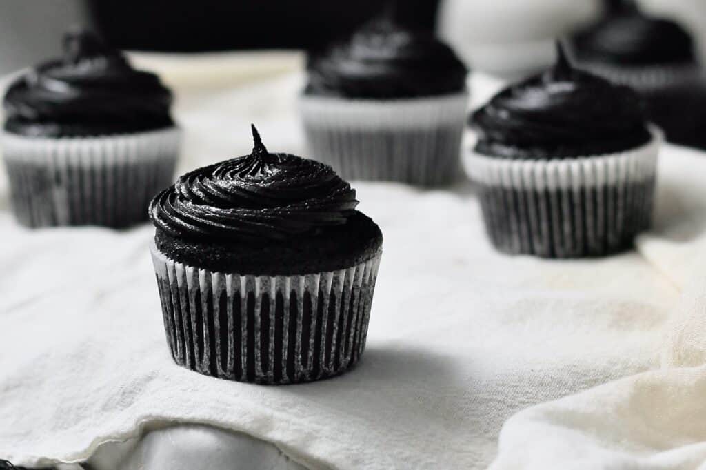 horizontal image of black velvet cupcakes, sitting on white linen