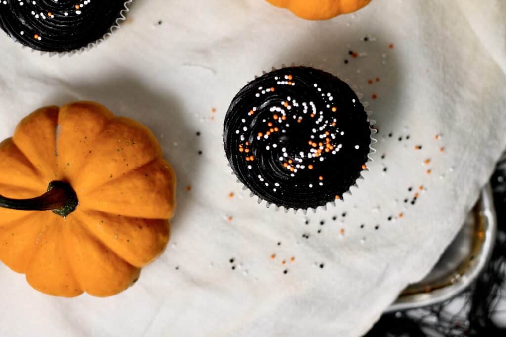 overhead image of black velvet cupcakes, surrounded by Halloween sprinkles and mini pumpkins