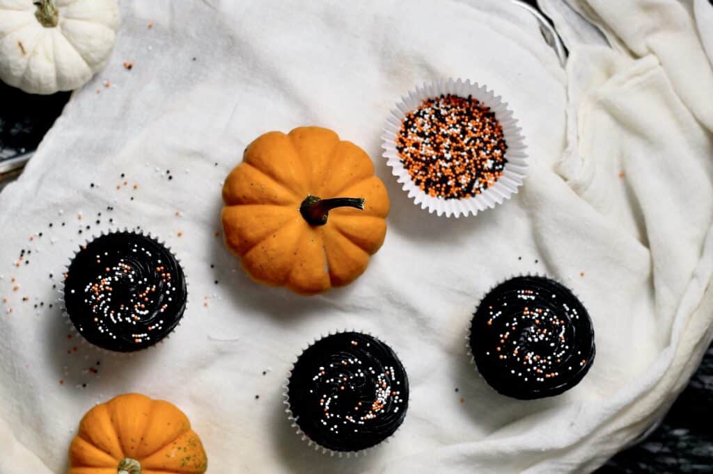 overhead image of black velvet cupcakes, surrounded by Halloween sprinkles and mini pumpkins