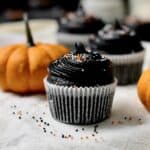 black velvet cupcake in the foreground, sitting on a baking tray, with a pumpkin and more black cupcakes behind it