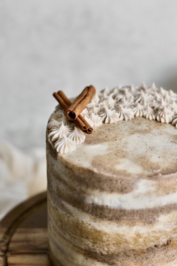 up-close image of dirty chai spice cake, coated in marbled frosting, with two cinnamon sticks on top, and sitting on a wooden cake stand