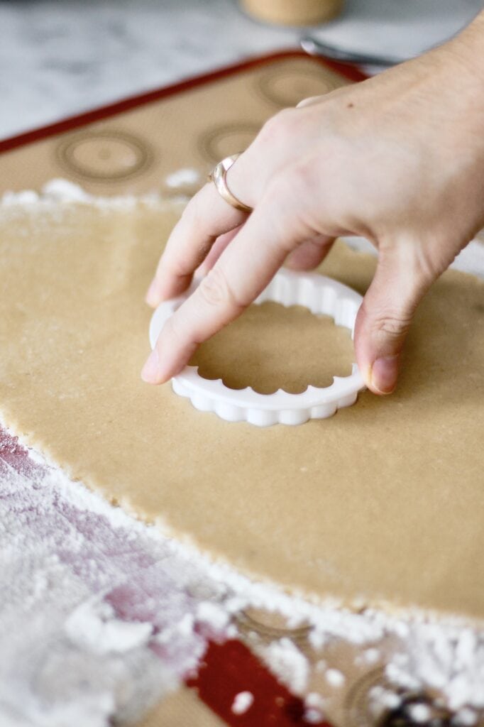 cutting out the wreath sugar cookies with a scalloped round cookie cutter
