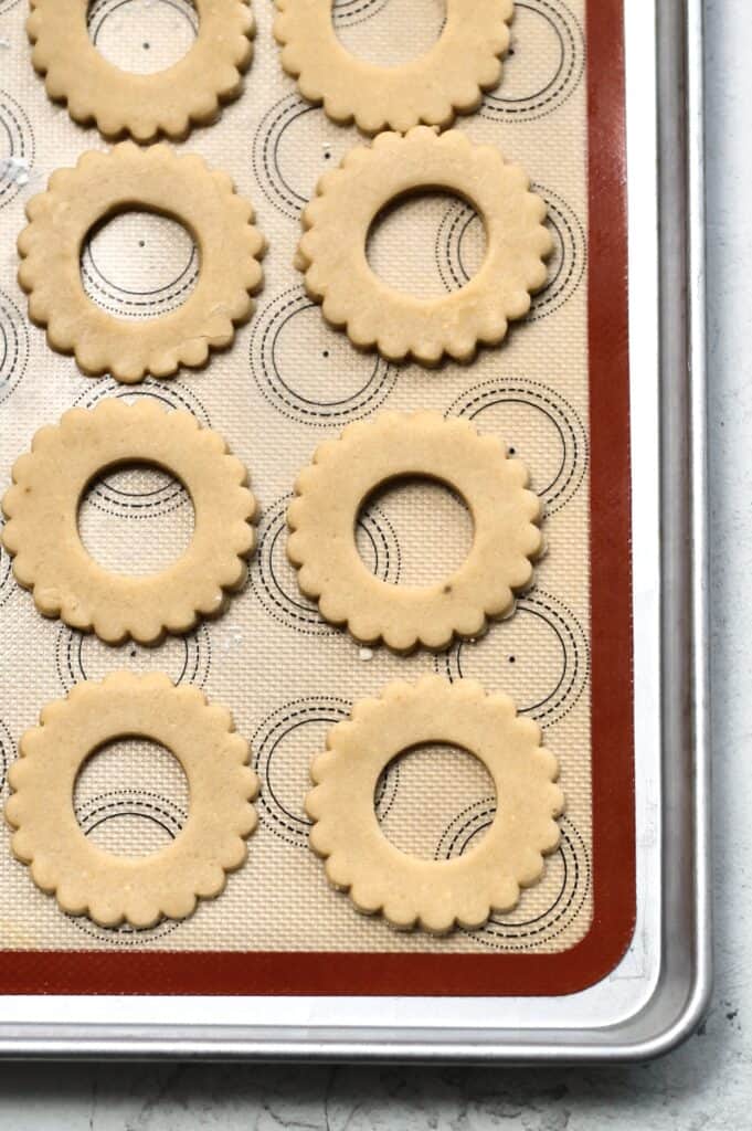unbaked Christmas wreath sugar cookies, sitting on a silicon mat atop a cookie sheet