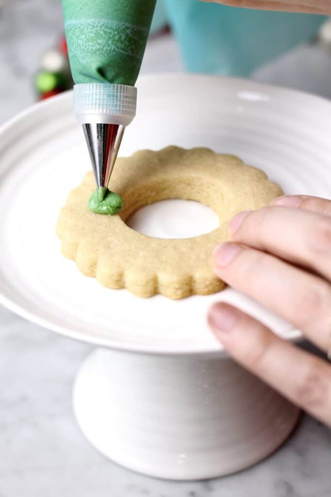 decorating wreath sugar cookies with a leaf tip and green buttercream
