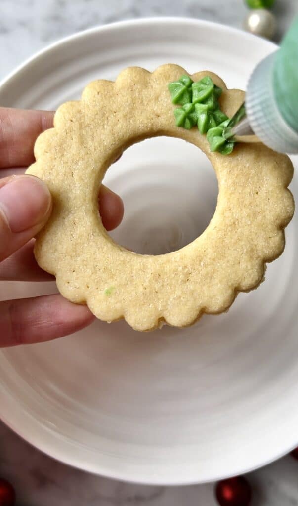 with a small open star tip, piping green buttercream onto a round, wreath cookie
