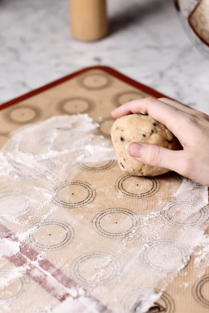 ball of chocolate chip sugar cookie dough on a silicon mat with a hand holding the ball