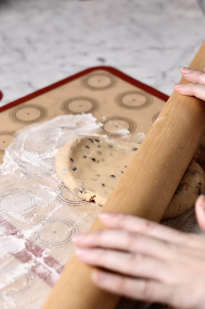 using a rolling pin to flatten ball of chocolate chip sugar cookie dough on a silicon mat