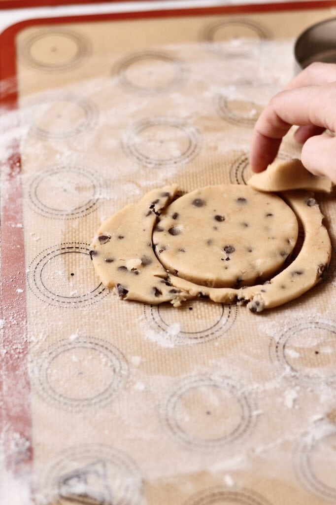 hand tearing away dough from cookie cutter to cut chocolate chip sugar cookies in round shapes on a silicon mat