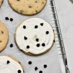 up-close image of frosted and unfrosted chocolate chip sugar cookies sitting on a wire rack with parchment paper on top of it