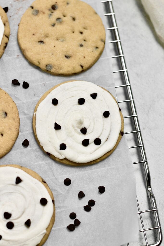 up-close image of  frosted and unfrosted chocolate chip sugar cookies sitting on a wire rack with parchment paper on top of it