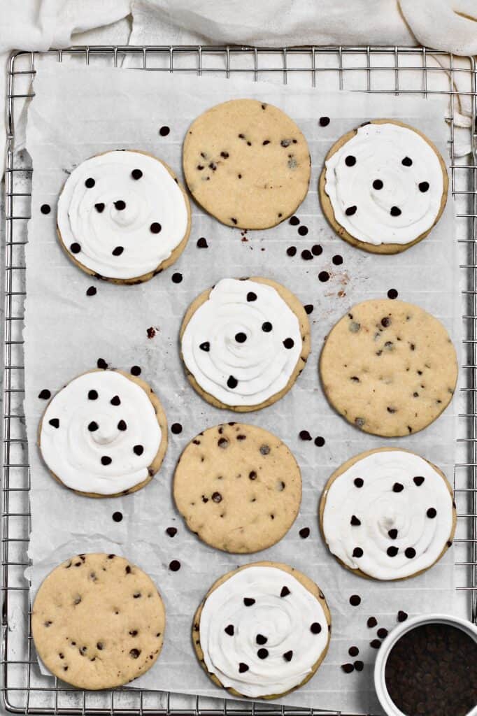 overhead image of frosted and unfrosted chocolate chip sugar cookies sitting on a wire rack with parchment paper on top of it