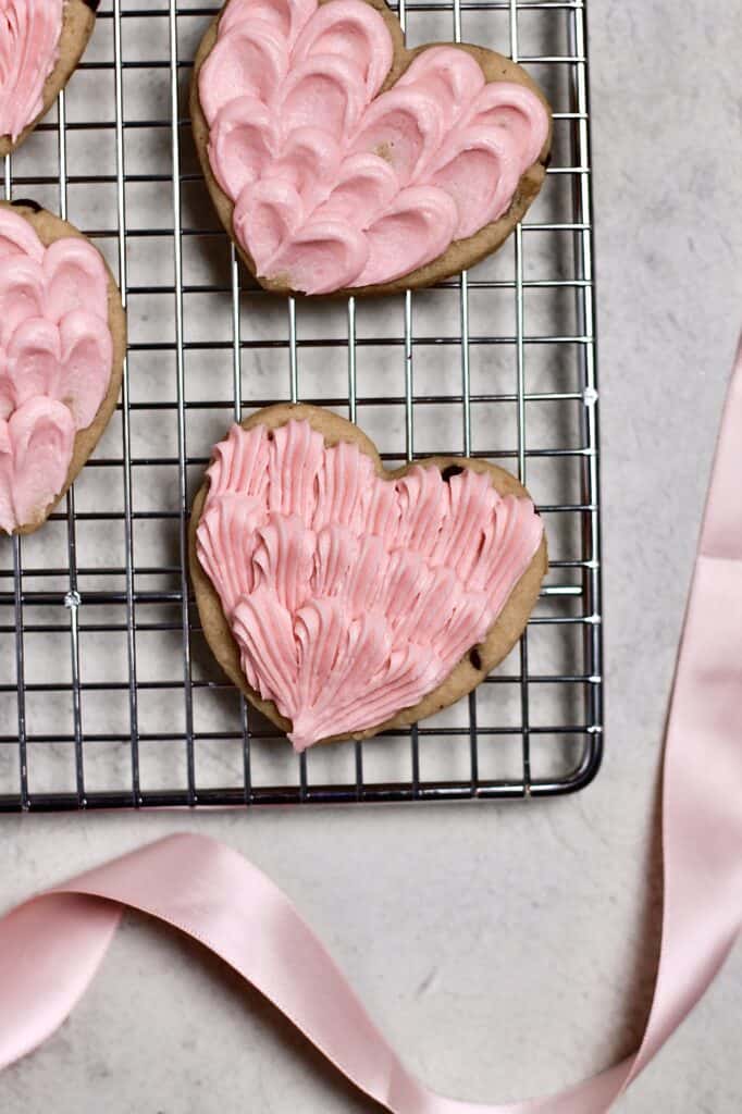 pink frosted cookies, in the shapes of hearts, sitting on a wire rack